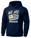 A navy blue pullover hoodie with a graphic print on the front. The design features the text 'WE ARE URUGUAY' in white and distressed black lettering, with a stylized, brush-stroke version of the Uruguayan flag in the center containing blue and white stripes and a yellow sun.