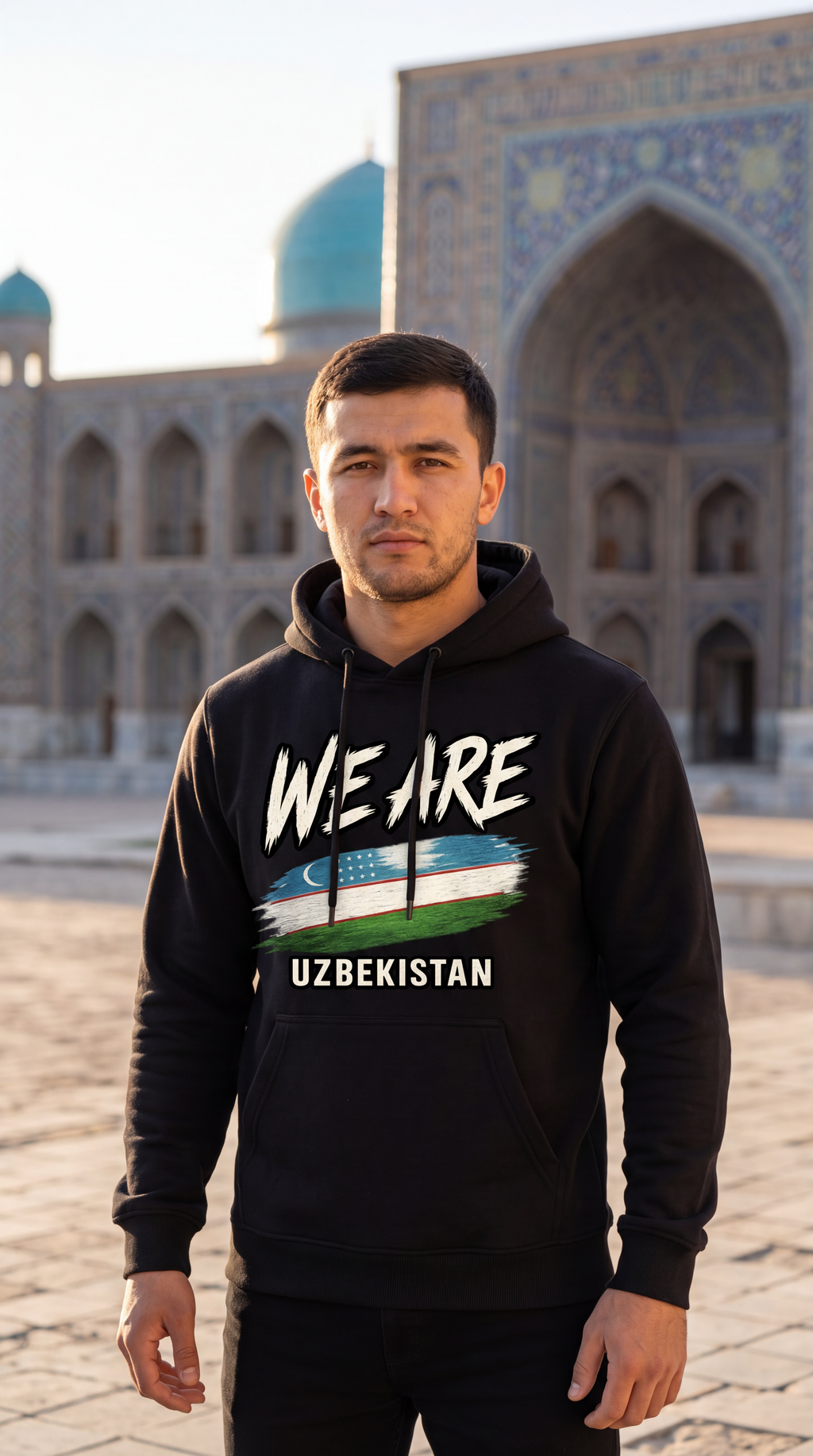 A man wearing a black hoodie with a graphic print of the Uzbek flag and the text 'WE ARE UZBEKISTAN' stands in front of a historic tiled building with blue domes.