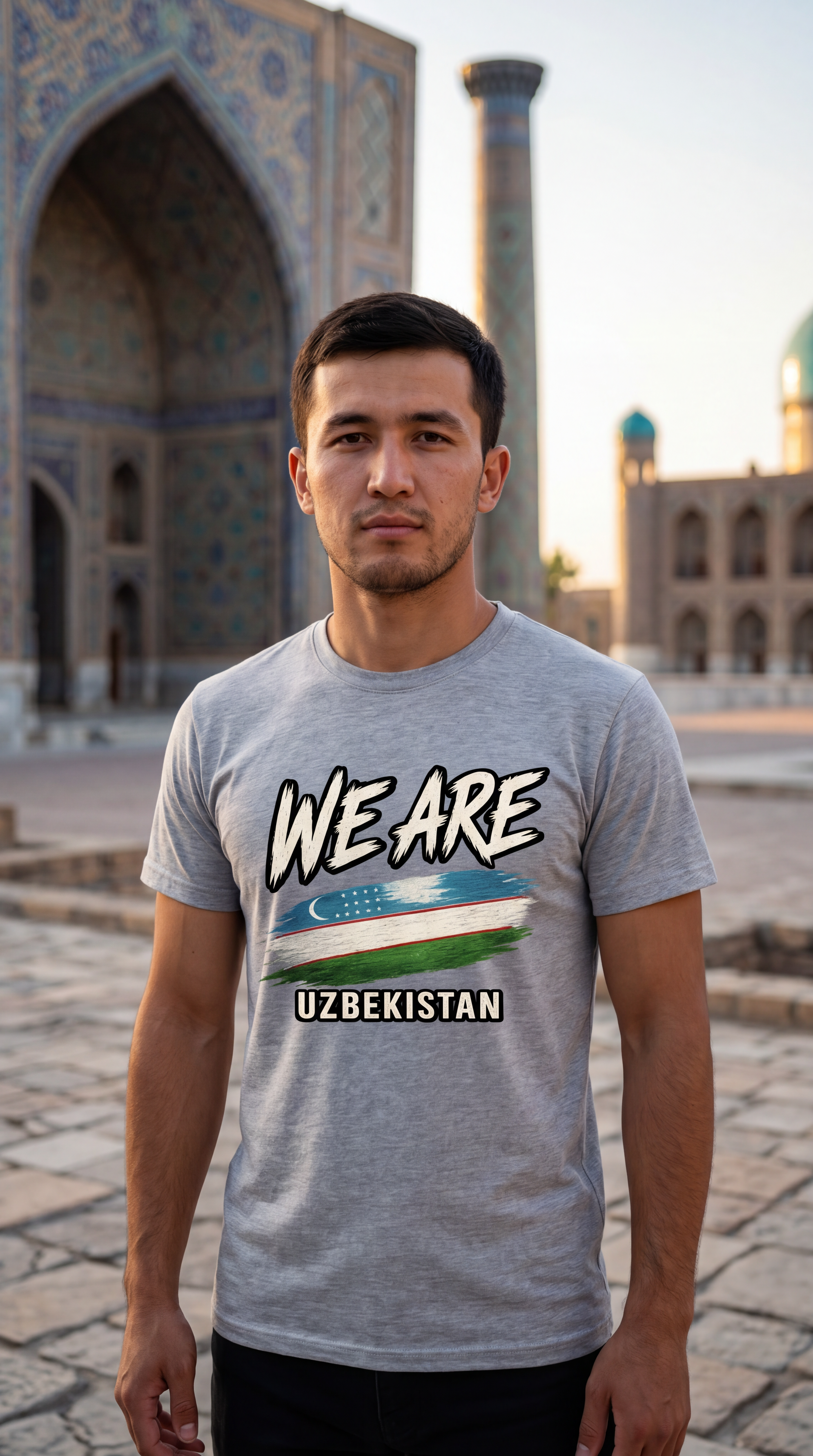 A man wearing a heather gray graphic t-shirt with 'WE ARE UZBEKISTAN' and the Uzbek flag printed on the front, standing outdoors in front of a historic tiled mosque arch.