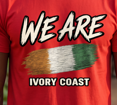 A close-up of a red t-shirt worn by a person, featuring a graphic print with the text 'WE ARE' in white brush lettering, a horizontal tricolor flag design in gold, white, and green, and 'IVORY COAST' below in white with black outlines.