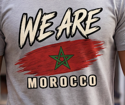 Close-up of a light gray t-shirt featuring a graphic print with the text 'WE ARE MOROCCO' and a red brushstroke background with a green star.