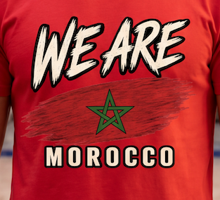 A close-up of a red t-shirt featuring a graphic print with the text 'WE ARE MOROCCO' and the green Moroccan star emblem.