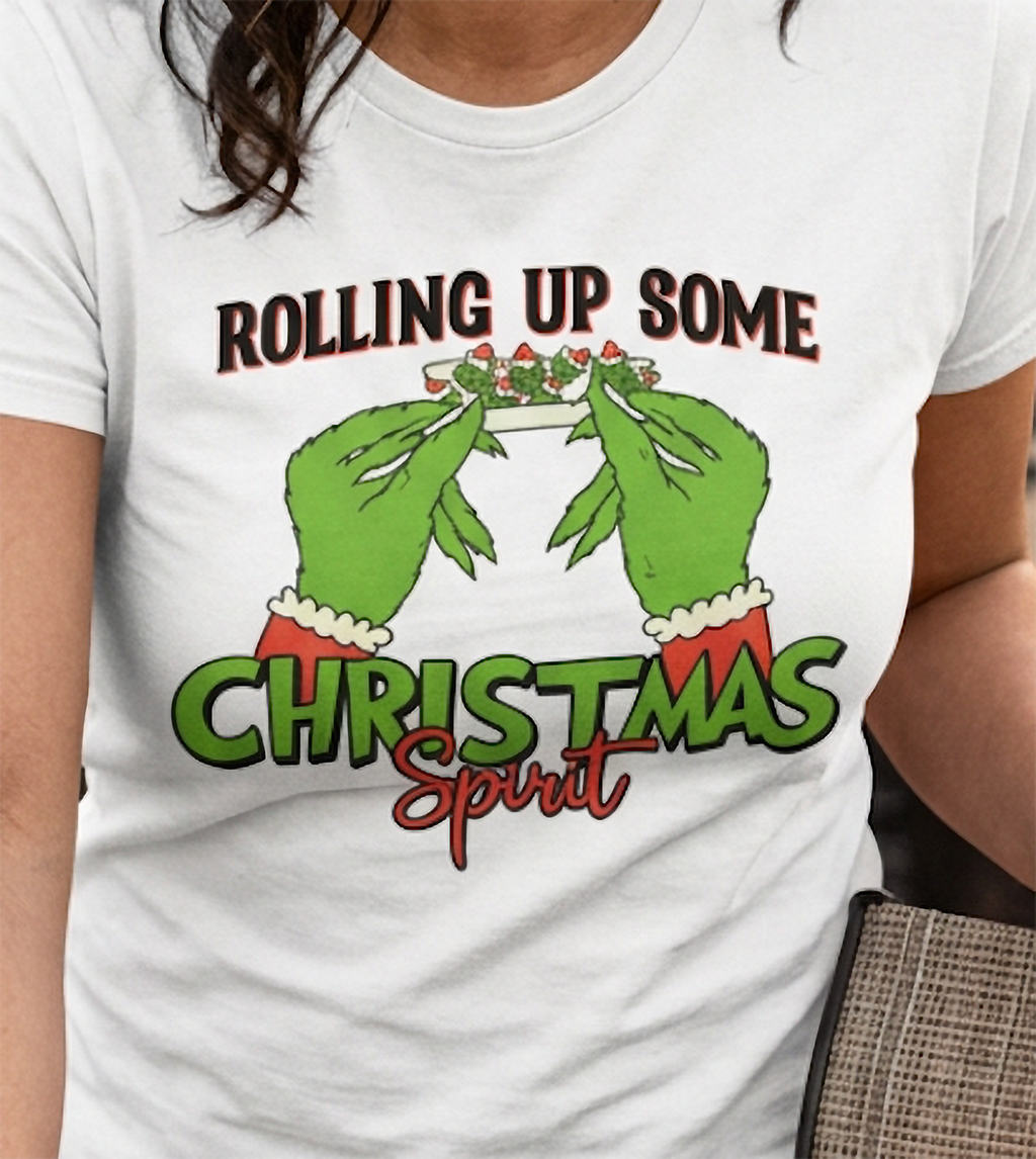 Close-up of white stoner Christmas t-shirt showing green hands rolling a holiday joint with bold Christmas lettering.