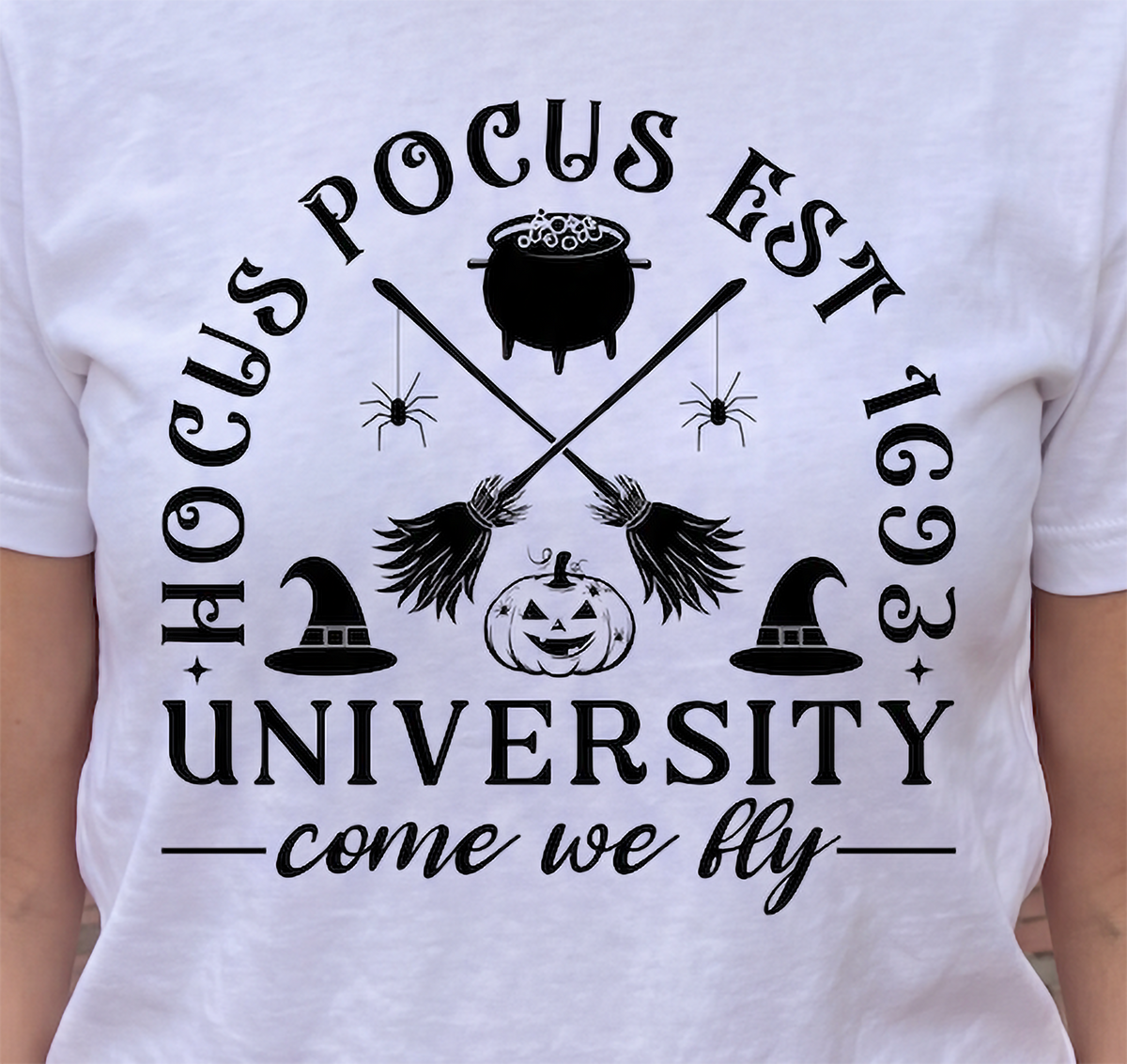 Close-up of white Hocus Pocus University Halloween shirt with broomsticks and cauldron