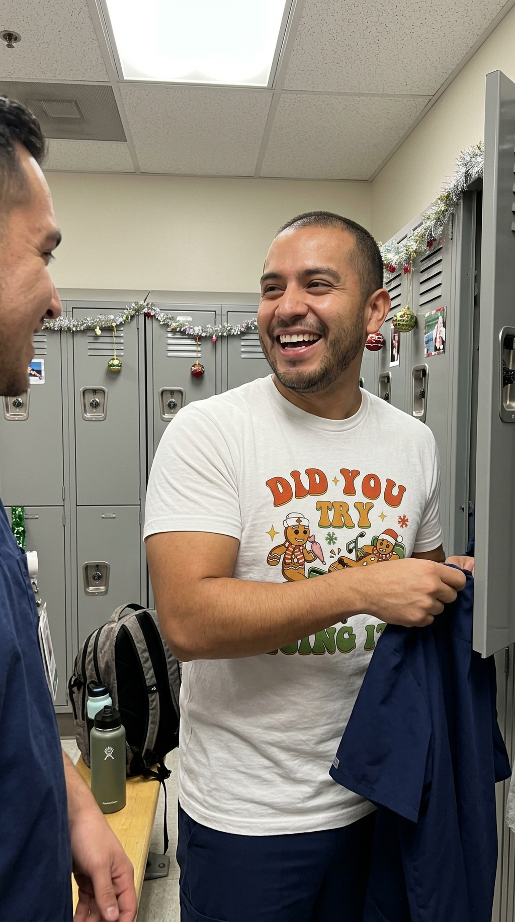 Man wearing a white gingerbread Christmas nurse t-shirt while carrying clothing in a healthcare workplace.