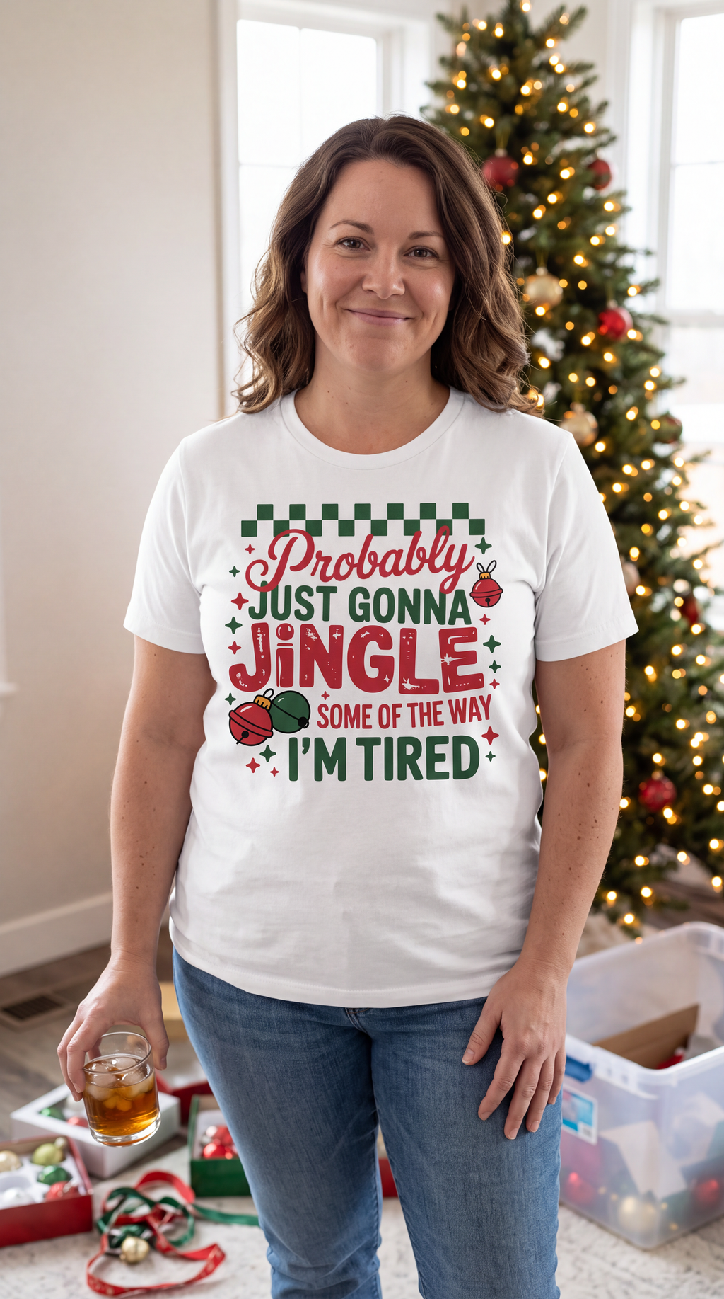 Woman wearing a white Probably Just Gonna Jingle Some of the Way Christmas shirt beside a decorated Christmas tree.