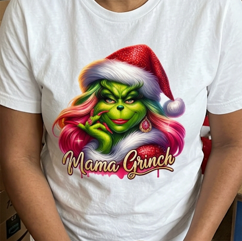 Close-up of white Mama Grinch Christmas t-shirt featuring colorful pink hair, green face and gold holiday lettering.
