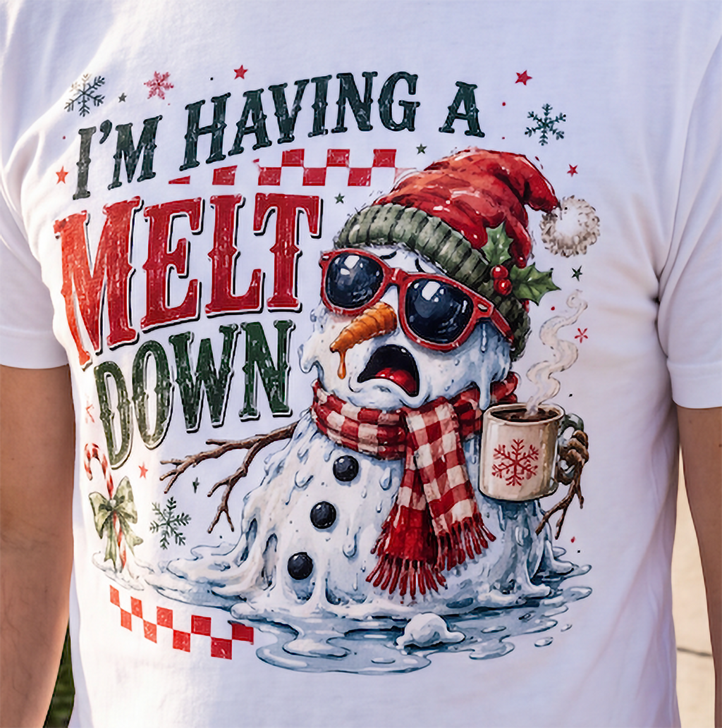 Close-up of white I’m Having a Meltdown Christmas graphic tee with snowman, plaid scarf and steaming holiday drink.