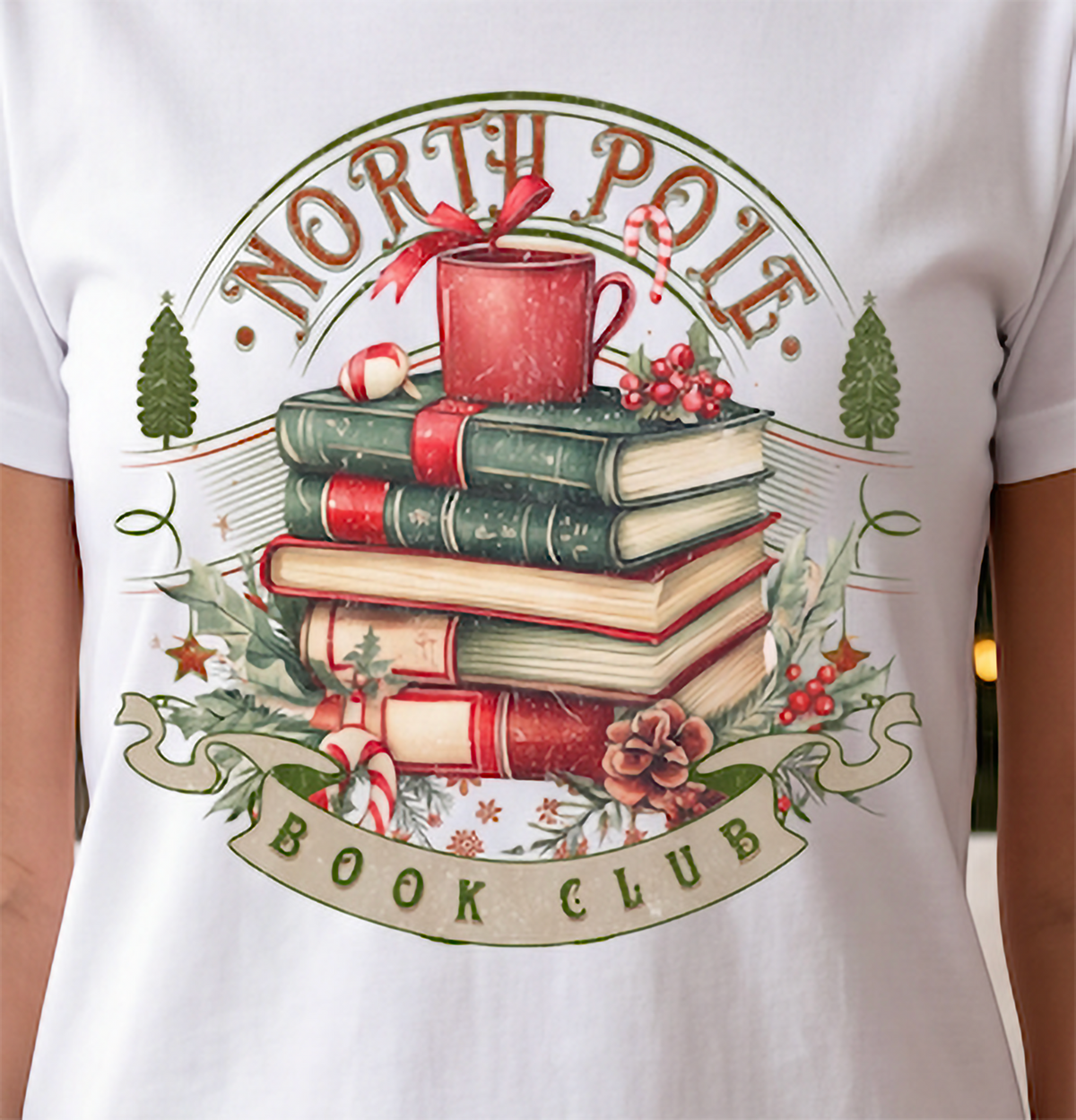 Close-up of North Pole Book Club graphic on white Christmas shirt with festive books, mug, holly and candy cane design.