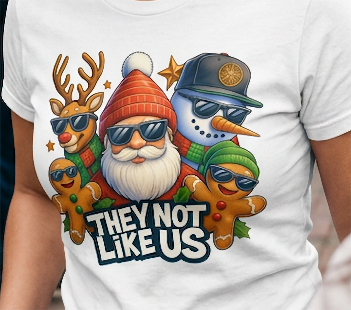 White Close-Up: Close-up of They Not Like Us Christmas design on a white t-shirt featuring Santa, a snowman, reindeer, and gingerbread characters wearing sunglasses.