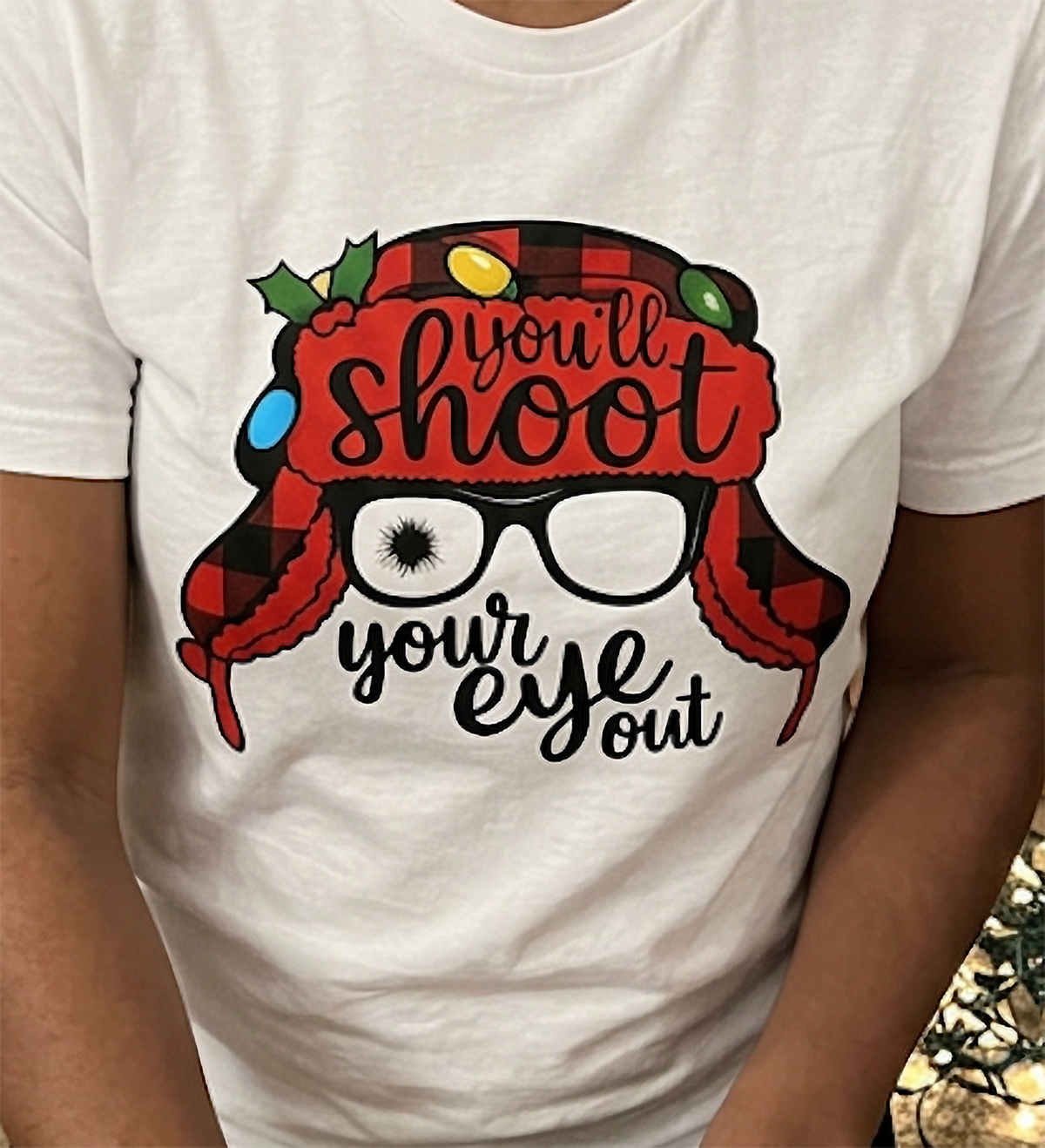 Close-up of white Christmas graphic t-shirt showing You'll Shoot Your Eye Out quote and festive buffalo plaid design