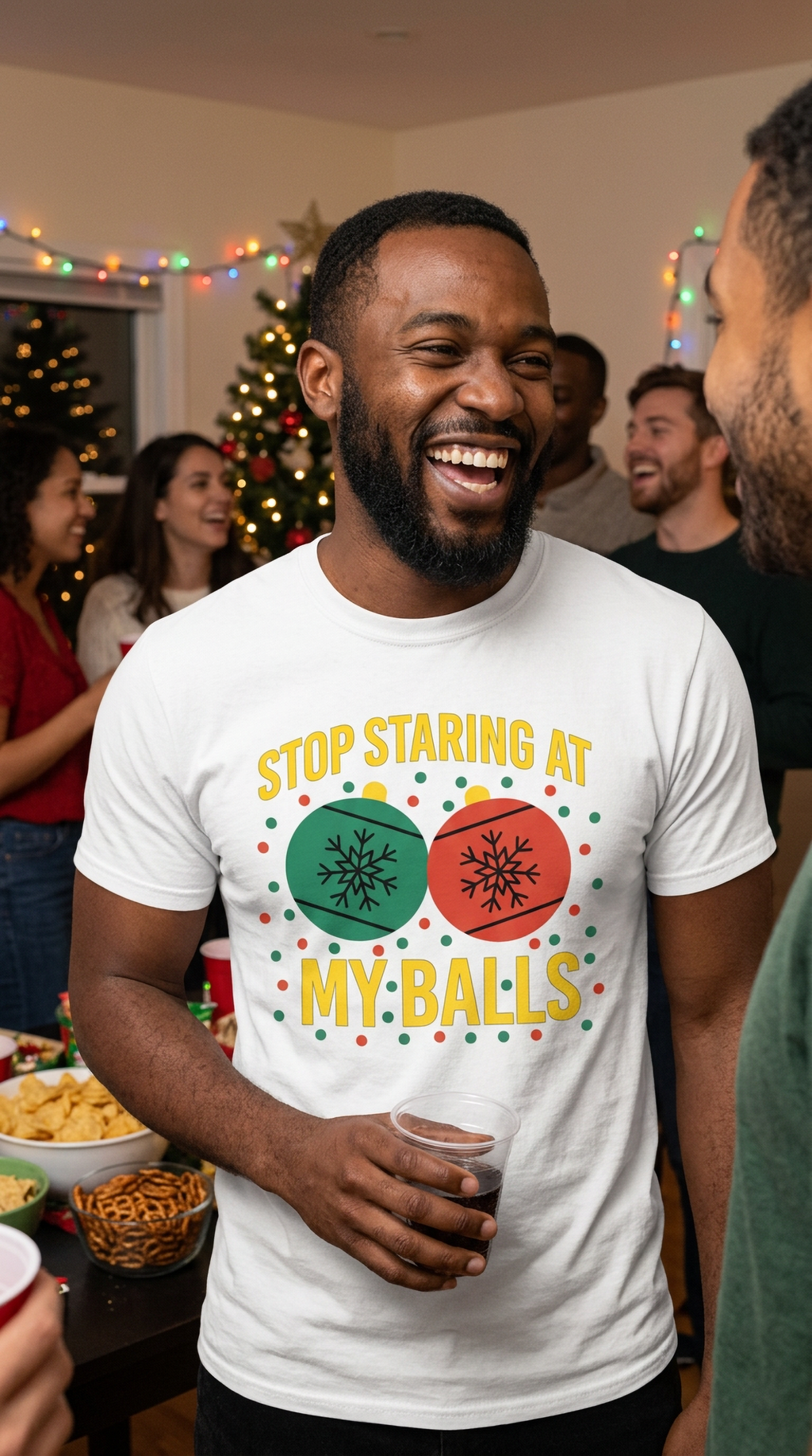 Smiling man wearing white Stop Staring at My Balls Christmas graphic tee at a festive holiday gathering.
