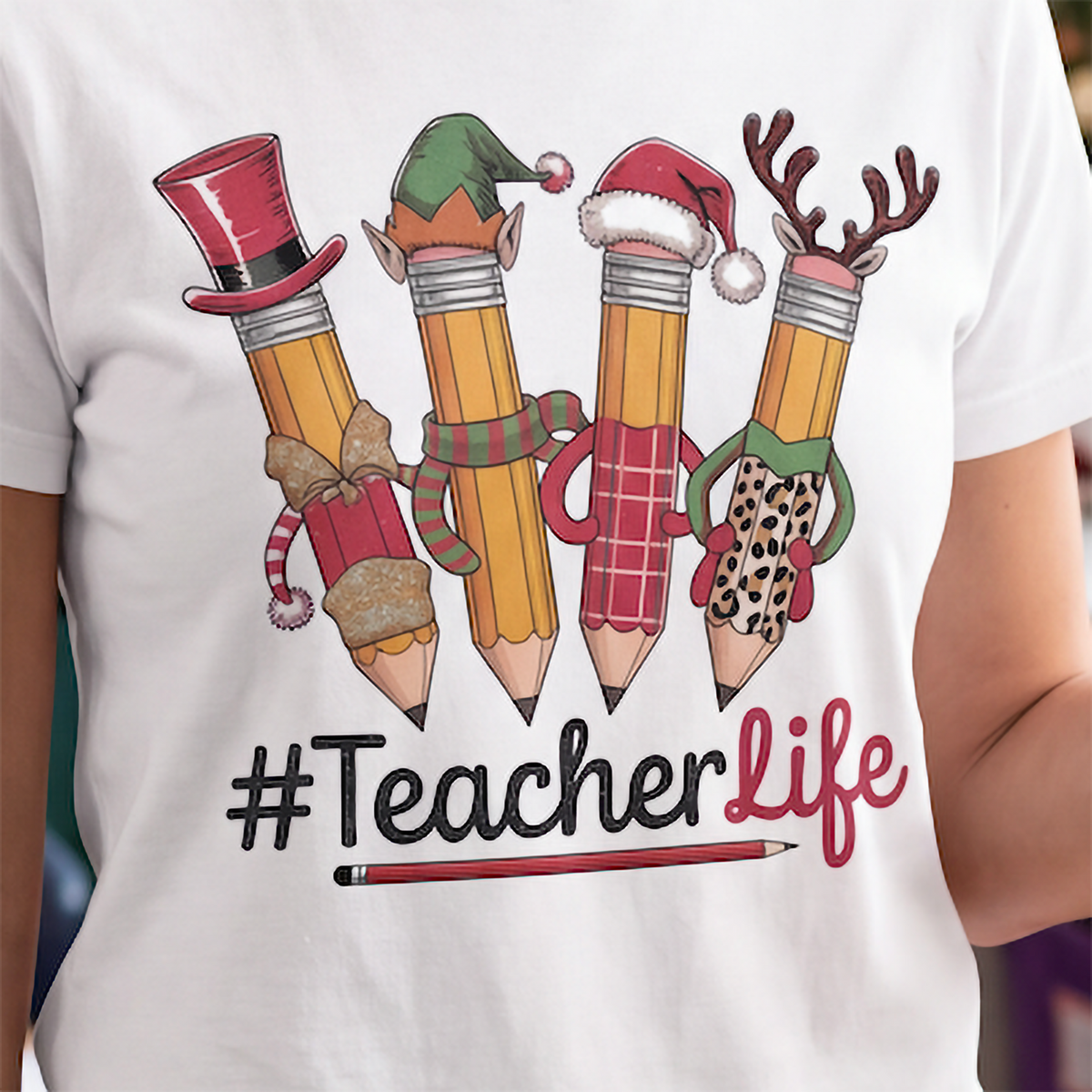 Close-up of white Teacher Life Christmas shirt with colorful festive pencils and #TeacherLife design.
