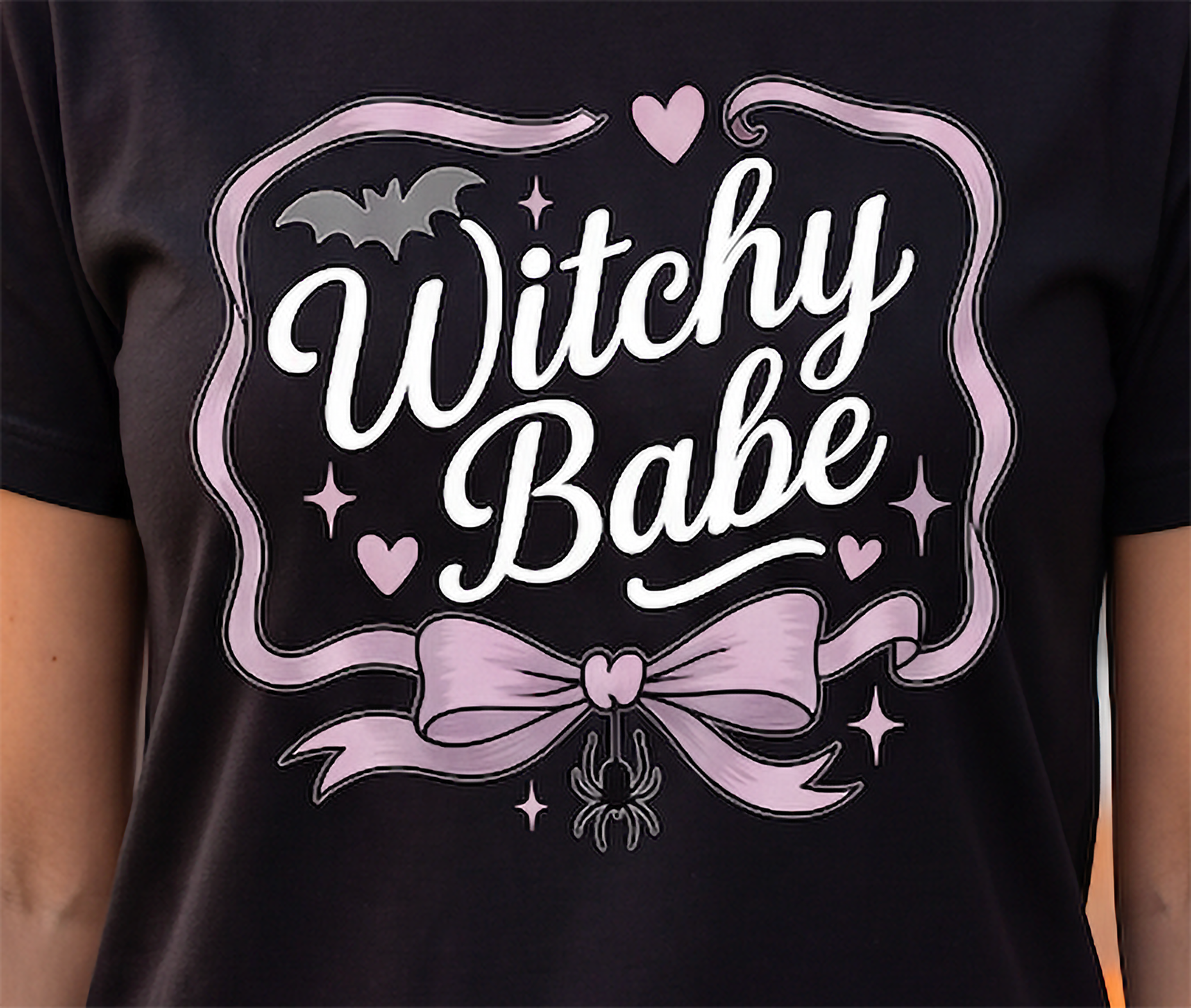 Close-up of Witchy Babe Halloween shirt graphic with pink bow, black bat, hearts, sparkles and spider