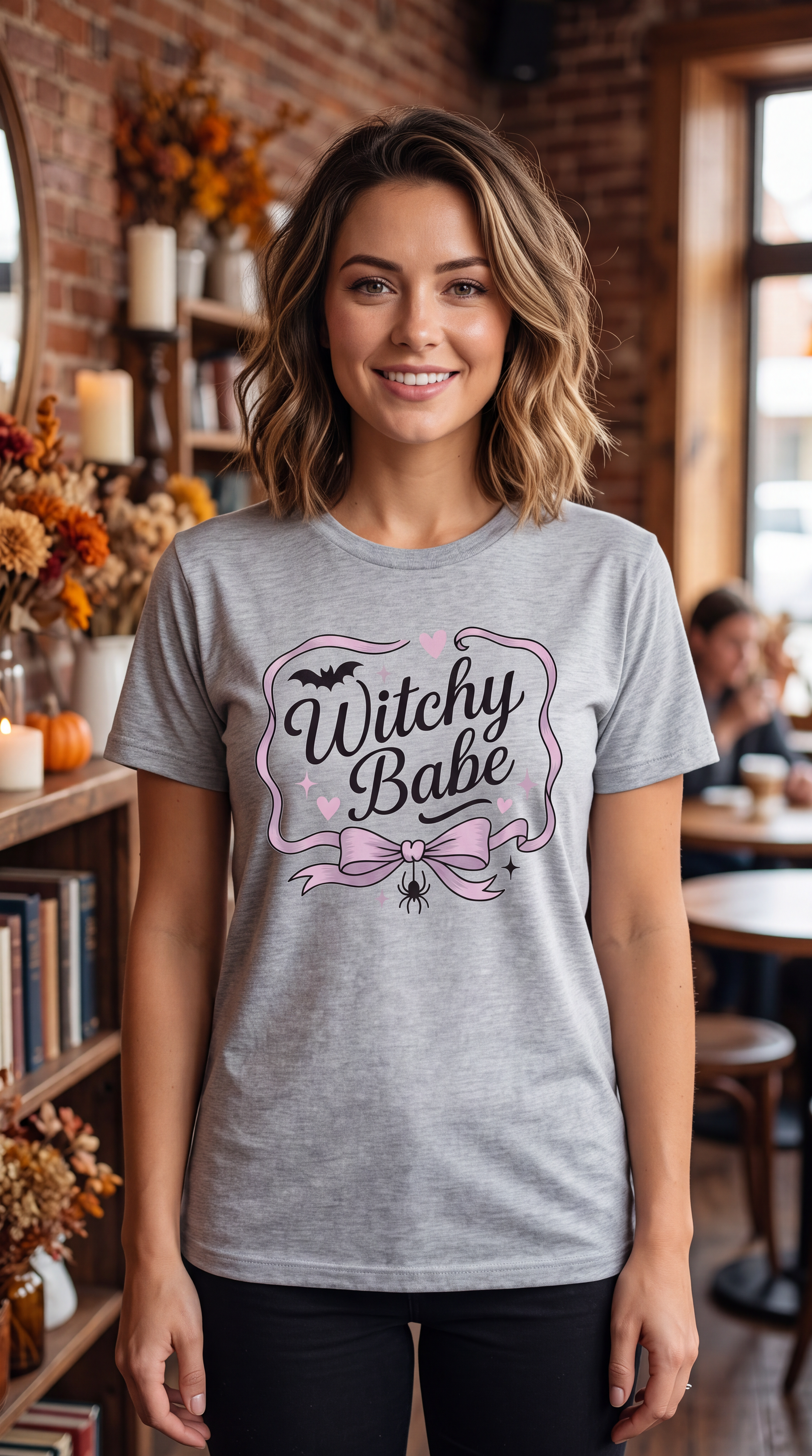 Woman wearing Heather Gray Witchy Babe Halloween shirt with feminine pink and black graphic in a fall cafe setting