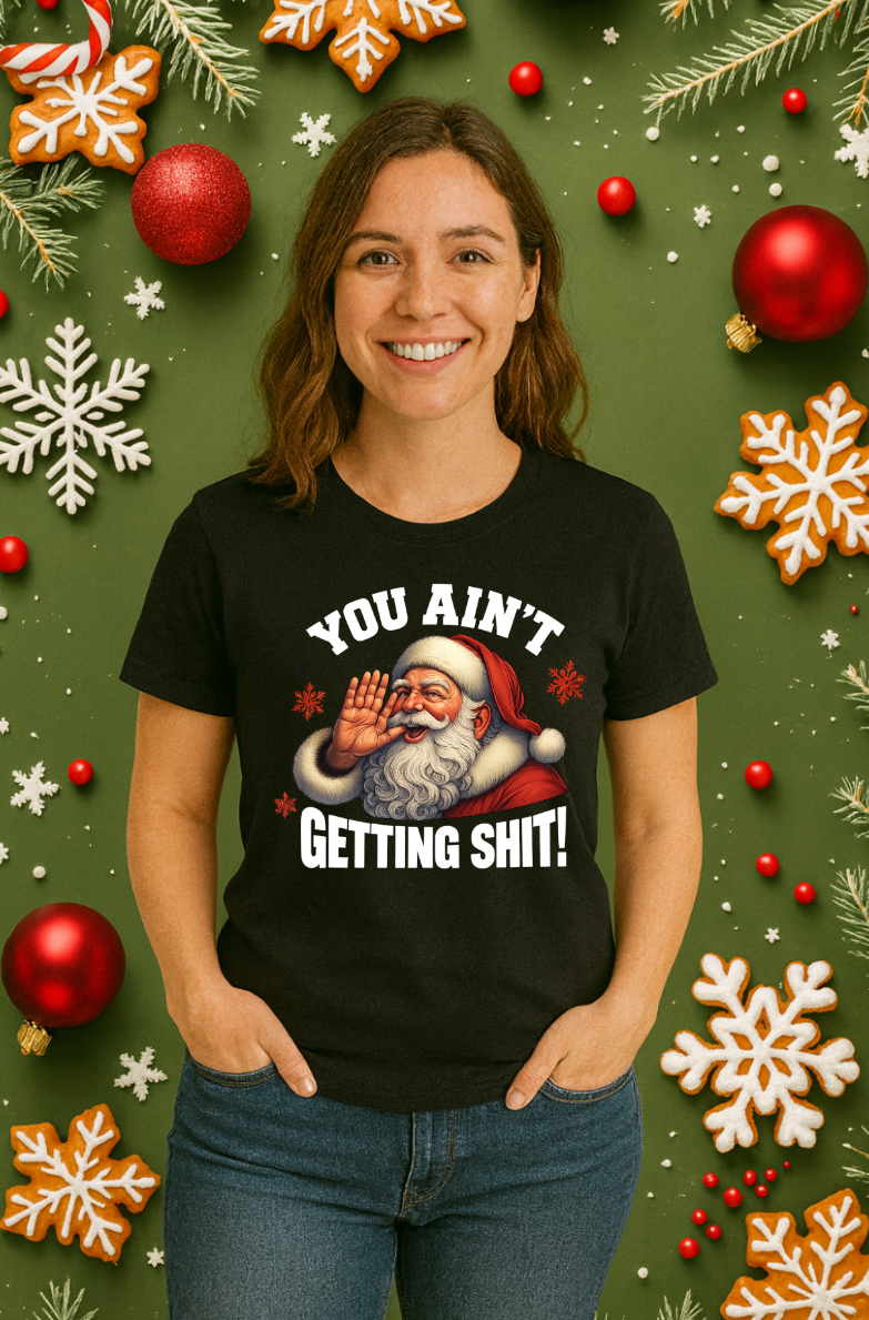 Woman wearing a black funny Christmas t-shirt with Santa Claus graphic and the phrase “You Ain’t Getting Shit,” standing against a festive holiday background with ornaments and snowflakes.
