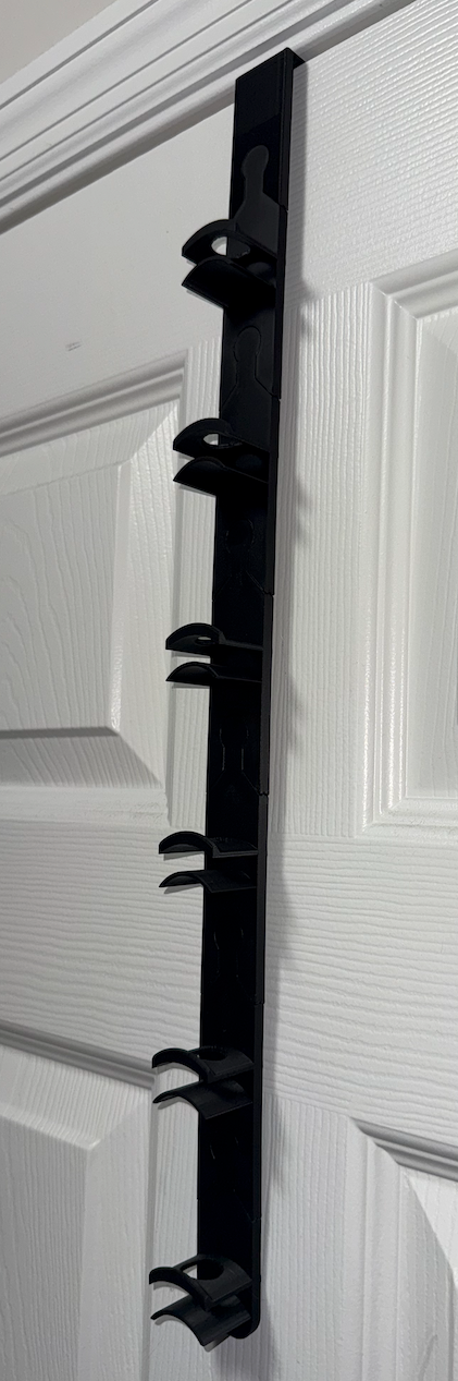 Black modular over-the-door hat rack organizer mounted on a white door for baseball cap, fitted hat, and snapback storage